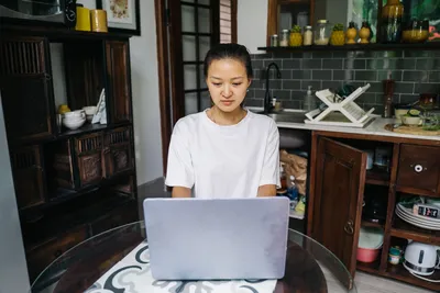A young woman working on her laptop in a cozy, well-organized kitchen, embodying a relaxed work-from-home environment.